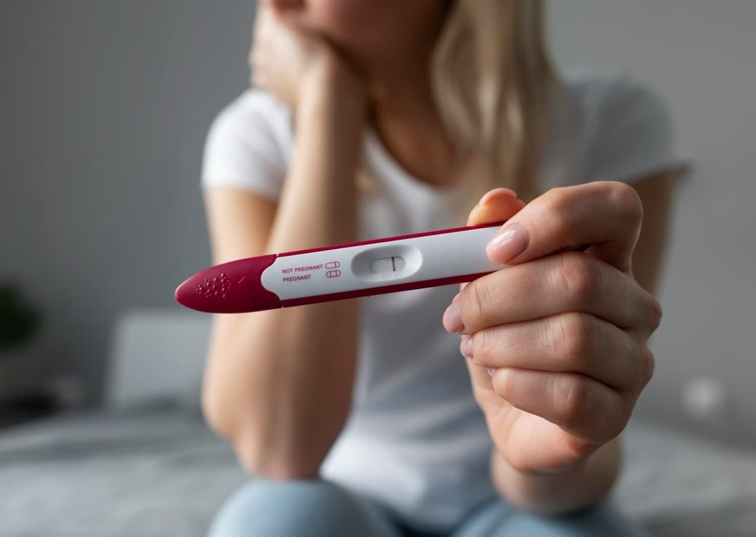 A woman holding a pregnancy test, contemplative